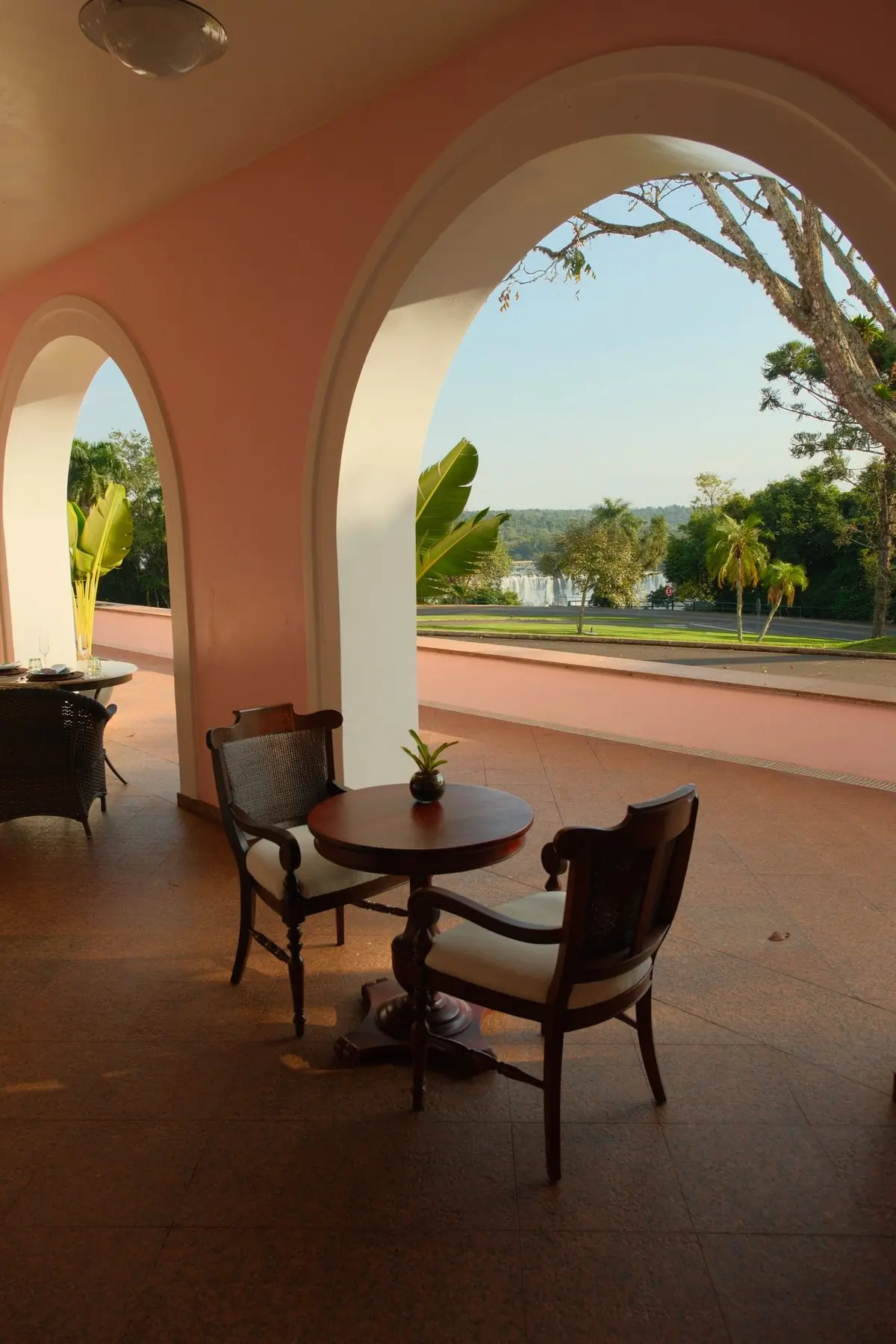 Pink arches and bistro tables on the hotel’s veranda bar, the falls visible through the arch