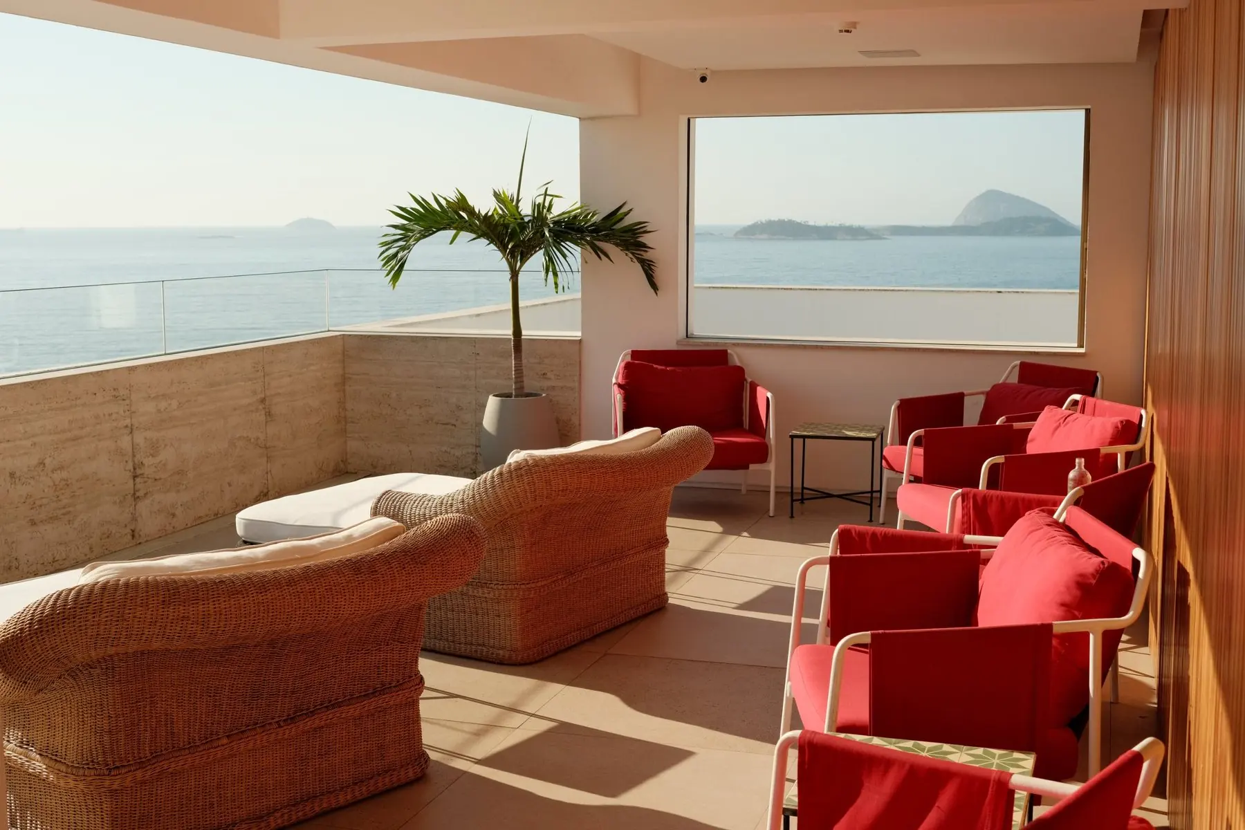 The rooftop lounge at Janeiro Hotel: wicker sofas, red armchairs and a framed view of the Cagarras islands