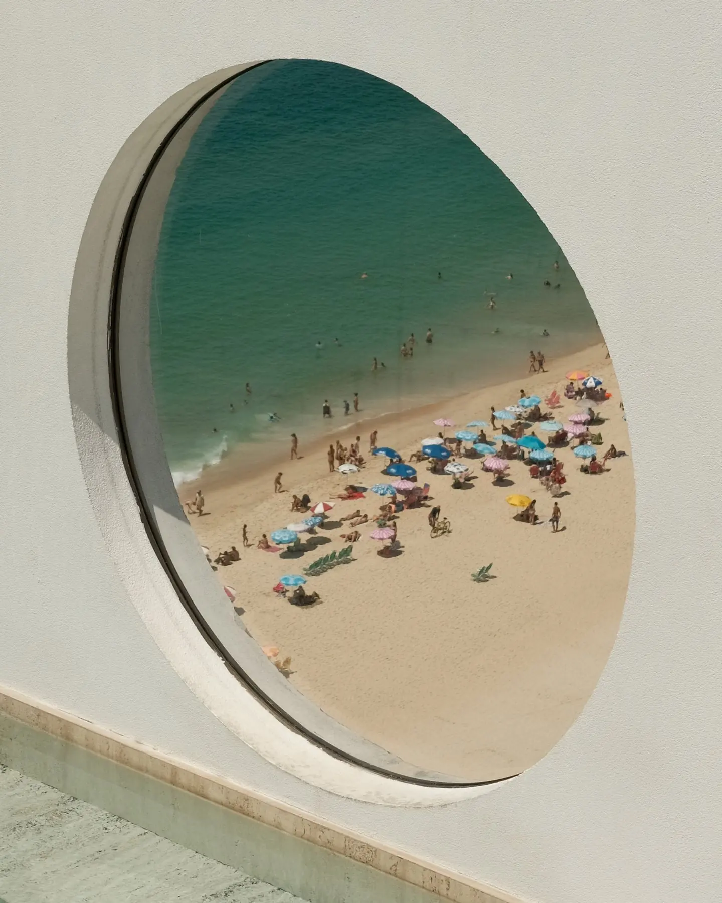 Leblon beach and its umbrellas seen from above through a round window in a white wall