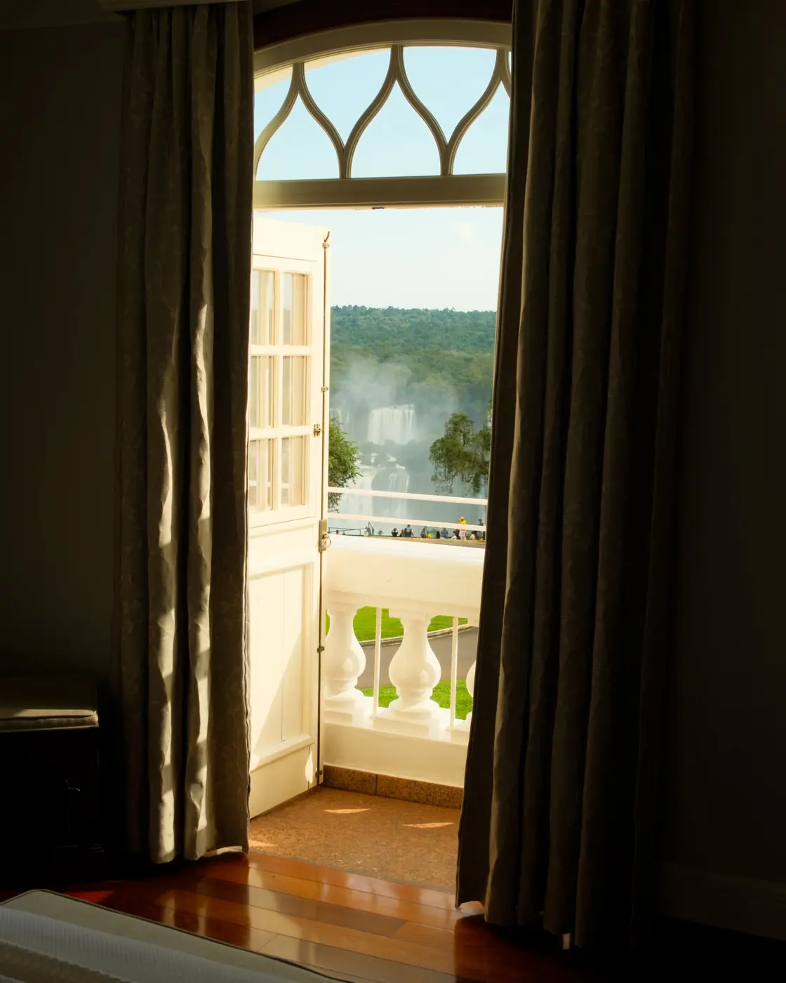Curtains drawn back in a guest room, the veranda balustrade and the falls’ mist beyond