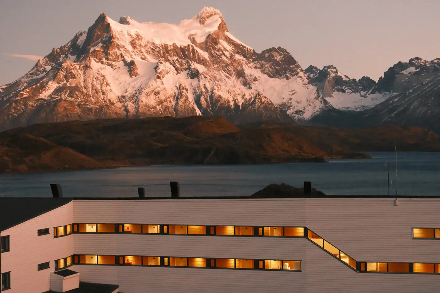 A guest room at dawn, its windows framing Paine Grande and the Cuernos above Lago Pehoé