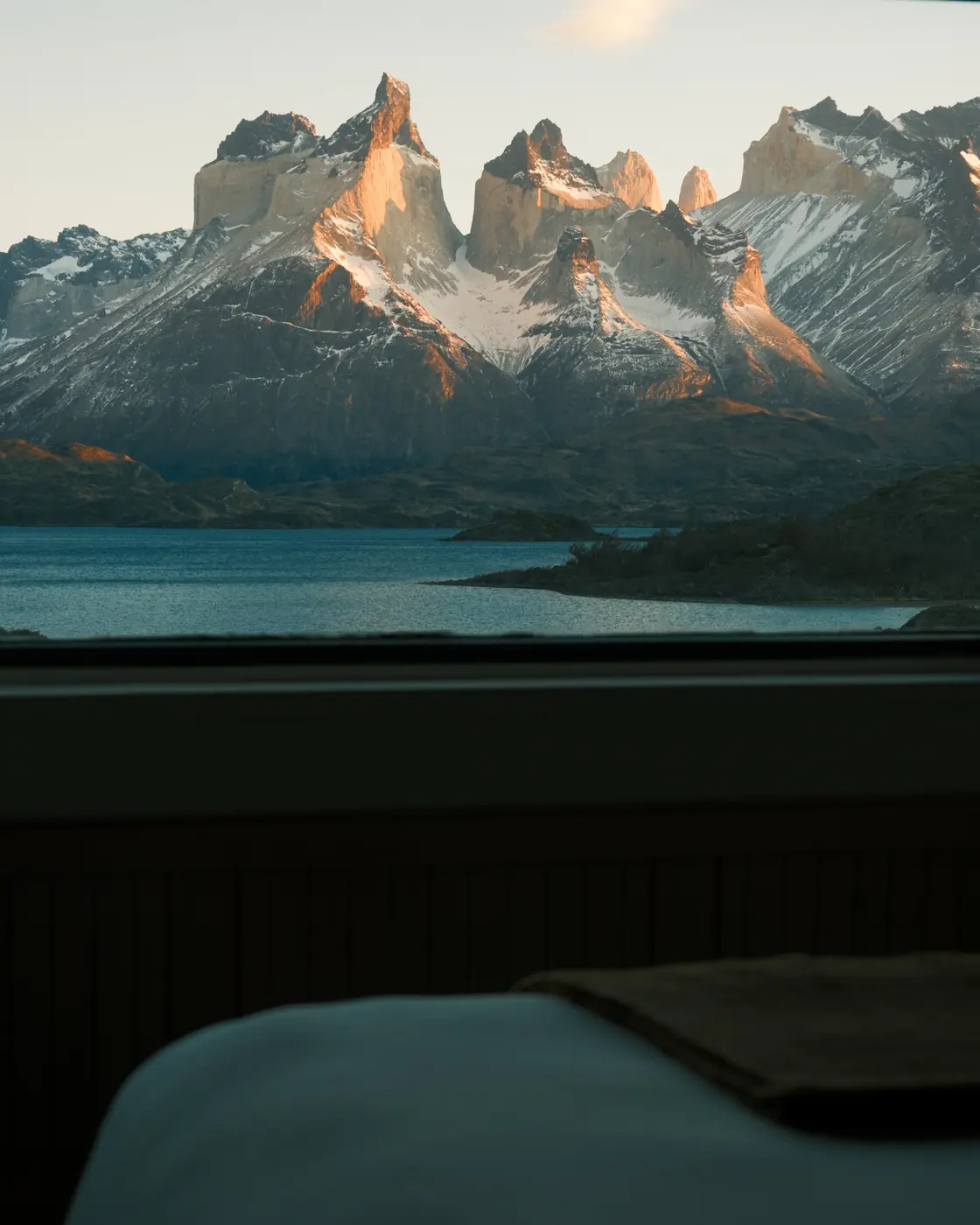 An armchair and a round table beside a window looking out at the Cuernos del Paine over Lago Pehoé
